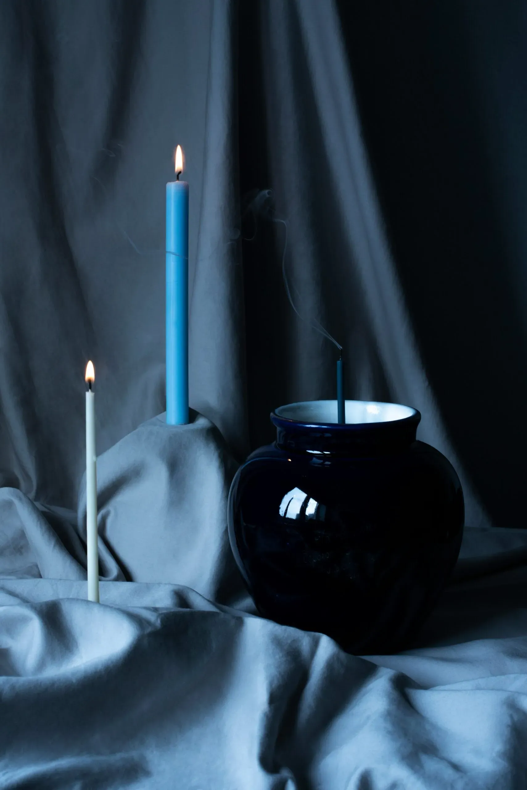 Chandelles allumées et vase bleu sur drapé sombre, ambiance de deuil.